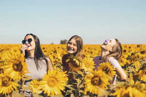 Group of girls in a field of sunflowers looking up at the sky showcasing Nöz's dermatologist recommended reef safe spf in it's unique color waves.